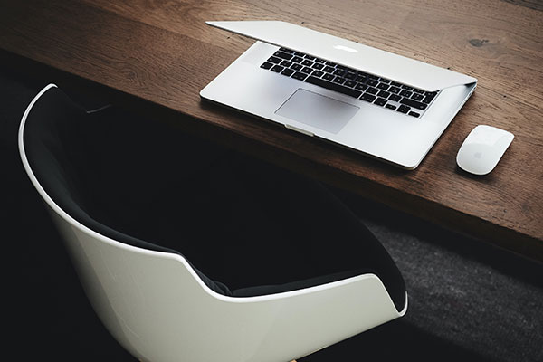 na biurku drewnianym laptop i myszka przy biurku stoi biało czarne krzesło